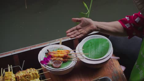 Down-Zoom-out-Shot,-Shrimp-on-a-stick-served-on-bamboo-leaves-prepared-by-a-boat-Vendor-in-Thailand-Floating-Market