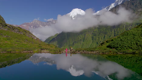 mesmerizing-drone-shot-reflects-lake,-greenery-Nepal-landscape-and-girl-wearing-pink-saree-enjoys-nature-4K