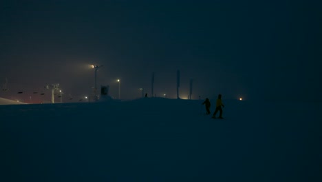 Aerial-drone-view-of-silhouette-skiers-at-slopes,-foggy-evening-in-gloomy-Lapland