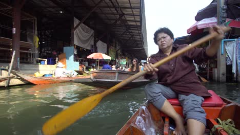 Mujer-Tailandesa-Remar-En-Barco-En-El-Tradicional-Mercado-Flotante,-POV-Cinematográfico,-Tailandia