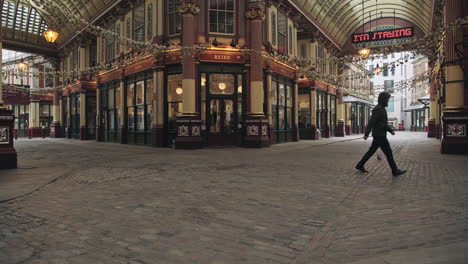 One-person-walking-in-an-empty-street-during-Coronavirus-Covid-19-lockdown-in-the-City-of-London-with-quiet-roads-and-shops-shut-and-closed-during-the-pandemic-at-Leadenhall-Market-in-England,-Europe