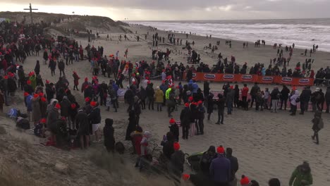 People-gathered-on-the-beach-ready-to-plunge-into-the-sea-for-New-Year's-dive---Wide-high-angle-static-shot
