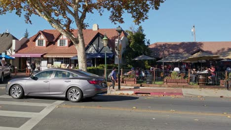 Cars,-an-old-windmill-and-people-at-a-restaurant,-in-the-Solvang-village,-California,-USA,-sunny-day---Pan-view
