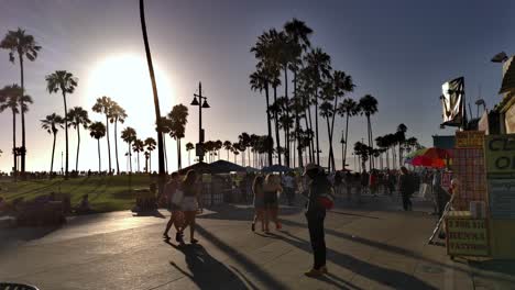 People-walking-around-the-Venice-Boardwalk-wearing-masks,-during-golden-hour,-in-Los-Angeles,-California,-USA---Quiet-do-to-the-Coronavirus-pandemic---Handheld-static-shot