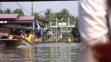 Barcos-Con-Turistas-Navegando-Por-El-Río-En-La-Entrada-Del-Mercado-Flotante-Tradicional,-Tailandia,-Punto-De-Vista-De-Pasajeros-En-Cámara-Lenta