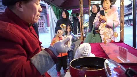 Auf-Einem-Kleinen-Jahrmarkt-In-Der-Wasserstadt-Gubei-Stellt-Ein-Mann-Süßigkeitentiere-Her,-Die-Wie-Glas-Blasen,-Während-Kinder-Auf-Den-Beginn-Der-Chinesischen-Neujahrsfeierlichkeiten-Warten