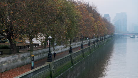 London-in-Coronavirus-Covid-19-lockdown-with-people-running-and-jogging-along-River-Thames-on-South-Bank-with-autumn-trees-on-atmospheric-misty-blue-morning-in-England,-UK-at-rush-hour