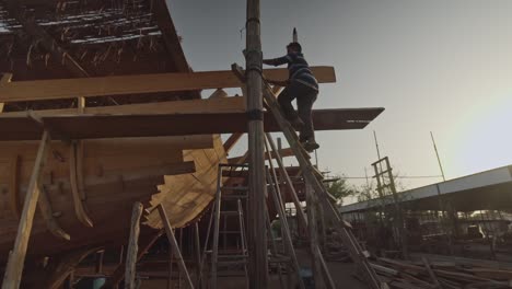 Trabajador-Subiendo-Una-Escalera-En-El-Astillero-De-Construcción-De-Barcos-Dhow-En-Sur,-Omán