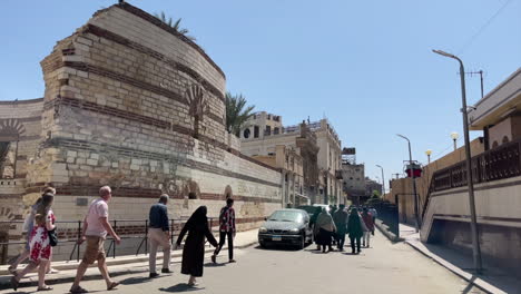 La-Gente-Camina-Delante-De-Los-Restos-De-Una-Torre-Romana-Junto-Al-Museo-Copto,-En-El-Cairo,-Egipto