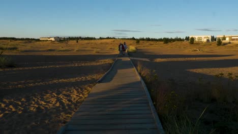 People-walking-on-duckboards,-summer-evening,-in-Kalajoki,-Finland---Handheld-view