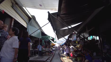 Walking-Down-on-Railway-Track-Between-Shops-on-Traditional-Market-in-Maeklong,-Thailand