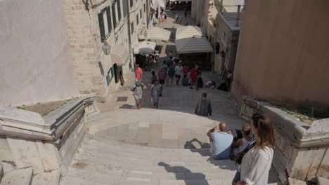 Stairs-of-Jesuit-and-narrow-street-with-many-tourist-and-bird-flying,-camera-tilting-up