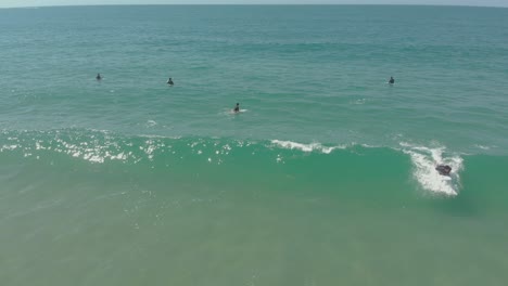 Luftaufnahme-Eines-Surfers,-Der-Eine-Welle-Fängt,-Während-Andere-Am-Praia-Do-Santinho,-Brasilien,-Auf-Die-Nächste-Welle-Warten-–-4k,-24-Fps