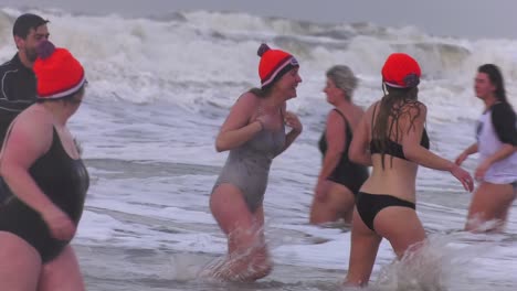 Happy-Dutch-women-leaving-the-sea-wet-and-cold-after-New-Year's-dive-in-Texel-Beach-in-North-Holland,-Netherlands---Close-Medium-Tracking-shot