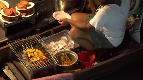 Palitos-De-Carne-Tailandesa-Y-Vendedora-Femenina-En-Barco-En-El-Mercado-Nocturno-Flotante-En-El-Campo-De-Tailandia
