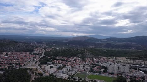 Drone-shot-flyng-backwards-over-the-town-of-Sibenik-and-the-mountains-in-background-under-a-cloudy-sky