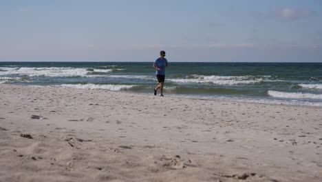 Young-adult-is-jogging-on-the-sandy-beach-of-Baltic-sea-in-the-beautiful-autumn-day,-Lithuania