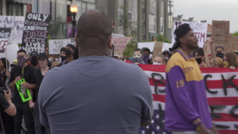 Ein-Mann-Beobachtet-Demonstranten-Der-Black-Lives-Matter-Bewegung,-Die-Schilder-Hochhalten-Und-Sprechchöre-Rufen,-Während-Sie-Die-Kreuzung-In-Der-Innenstadt-Blockieren