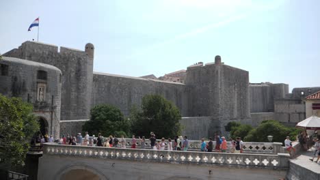 Majestätisches-Schloss-Von-Dubrovnik-Mit-Vielen-Touristen,-Die-Auf-Einer-Steinbrücke-Spazieren