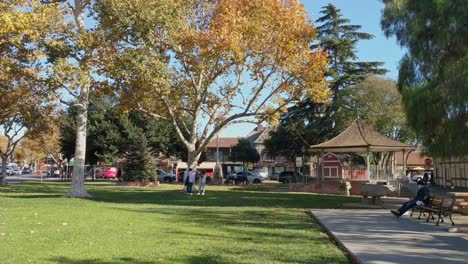 People-standing-in-the-park-and-sitting-on-benches-in-Solvang,-California-on-a-sunny-day-in-winter---Static-Shot