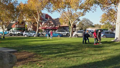 People-sitting-and-walking-around-in-a-park-on-a-sunny-day-in-Solvang,-California---Panning-Shot