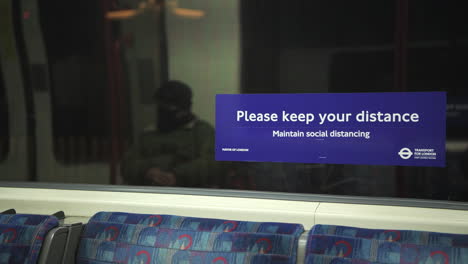 Person-wearing-face-mask-on-public-transport,-with-Covid-19-Coronavirus-information-sign-in-London-Underground-tube-train-carriage-for-social-distancing-in-England,-UK
