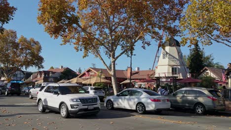 Cars-on-street-in-front-of-restaurants-and-a-windmill,-in-the-Solvang-village,-California,-USA,-sunny-day---Static-view