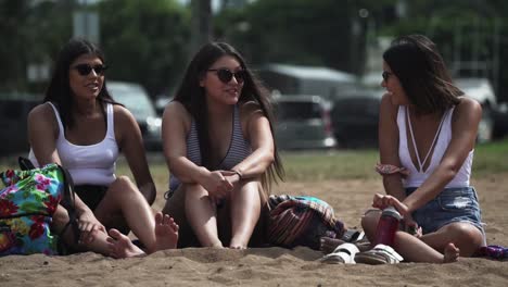 Three-carefree-Girls-talking-and-relaxing-sitting-by-the-beach-in-Oahu,-Hawaii---Medium-close-up-shot