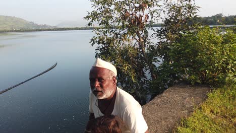 Grandfather-With-His-Grandchild-Sitting-On-The-Ground-With-Lake-In-The-Background