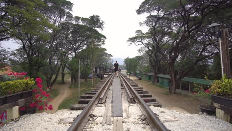 Walking-on-Railway-From-Station-Toward-River-Kwai-Bridge,-Landmark-From-WWII-and-Tourist-Attraction,-Thailand