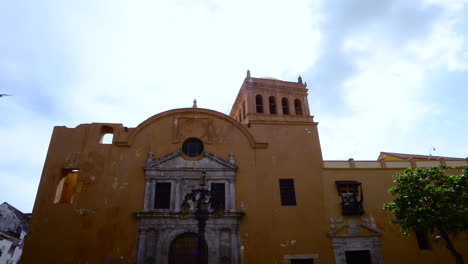 Hand-Held-Shot-of-catholic-Iglesia-de-Santo-Domingo-in-Cartagena-Colombia,-while-a-bird-passes-by-and-lands-on-the-ceiling-of-the-church-on-q-summer-afternoon
