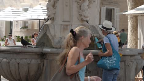 Pigeon-flies-away-while-woman-comes-to-fill-water-from-historical-fountain-in-Dubrovnik