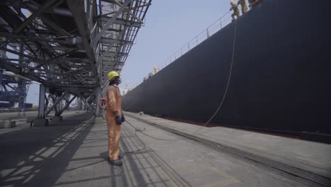 Dockworker-In-Hard-Hat-And-Mask-Holding-Mooring-Rope-Of-A-Big-Ship-At-The-Port