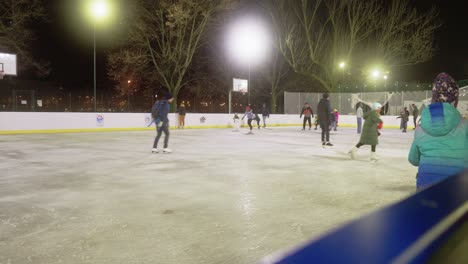 Several-people-are-enjoying-ice-skating-at-an-outdoor-ice-skating-rink-during-the-night