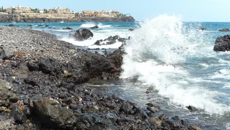 Resort-building-on-rocky-coast-of-Tenerife-with-flowing-ocean-waves,-slow-motion