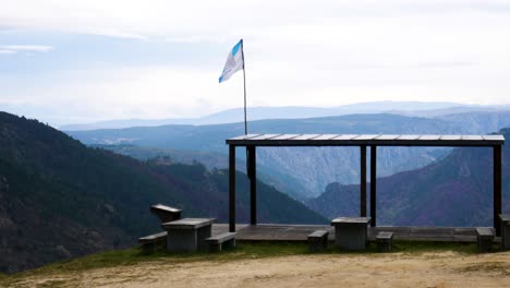 Pan-across-scenic-overlook-with-shade-covering-and-benches-as-Spanish-flag-waves-in-wind