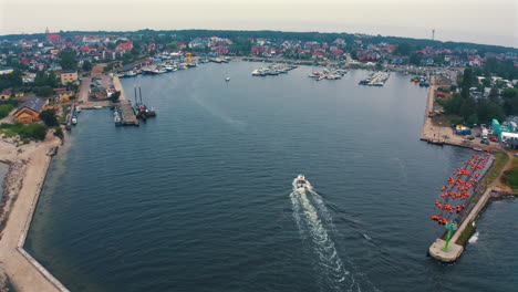 Aerial-view-of-motorboat-sailing-towards-the-marina-in-Jastarnia,-Poland-with-moored-yachts-in-the-background