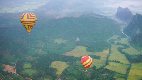 Pair-Of-Hot-Air-Balloons-Flying-Over-Green-Fields-In-Vang-Vieng,-Laos