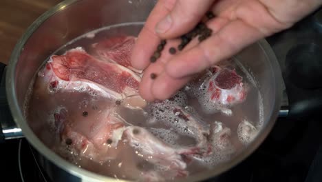 Hand-adding-whole-pepper-to-pot-with-beef-bones-for-broth,-close-up-slow-motion