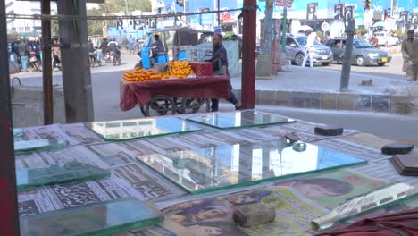 Rückwärts-Zeitlupenaufnahme-Eines-Straßenstandes-Eines-Mannes,-Der-An-Einem-Sonnigen-Nachmittag-In-Der-Saddar-Bazar-Street-In-Karatschi-In-Pakistan-Zeitung-Verkauft