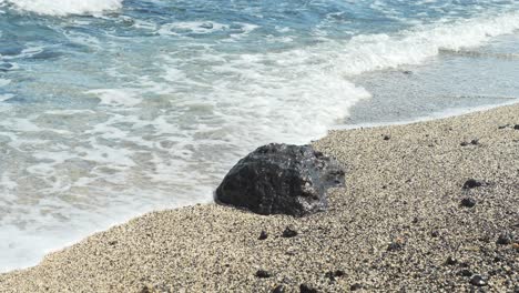 Lonely-stone,-sandy-beach-and-pure-ocean-water-flowing-over-in-Tenerife