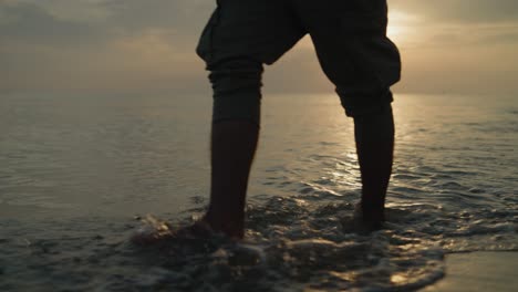 Mid-shot-of-Male-walking-on-the-beach-in-the-water-at-sunrise-towards-the-camera-slow-motion