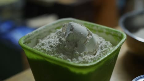Plastic-cup-full-of-plain-white-flour-tipped-into-green-plastic-container,-filmed-as-closeup-slow-motion-shot