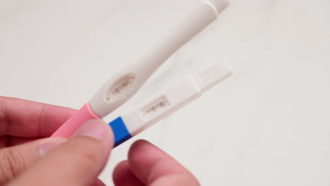 Close-up-of-an-individual-holding-two-kinds-of-home-pregnancy-test-kits,-one-colored-blue-and-another-one-colored-pink