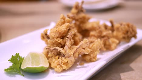 A-closer-shot-of-a-tasty-and-crispy-deep-fried-seafood-in-a-platter,-served-with-lime,-and-eaten-using-a-pair-of-chopsticks