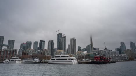 Zeitraffer-Eines-Bewölkten-Blicks-Auf-Die-Skyline-Von-Toronto-Mit-An-Der-Uferpromenade-Angedockten-Booten-Und-Vom-Nebel-Verdecktem-CN-Tower