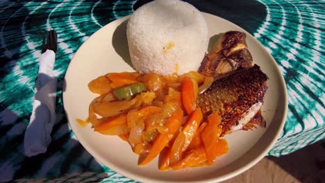 Würziger-Fisch-Yassa-Köstlicher-Afrikanischer-Teller-Auf-Dem-Tisch-Mit-Grünem-Batik-Tischblatt,-Nahaufnahme