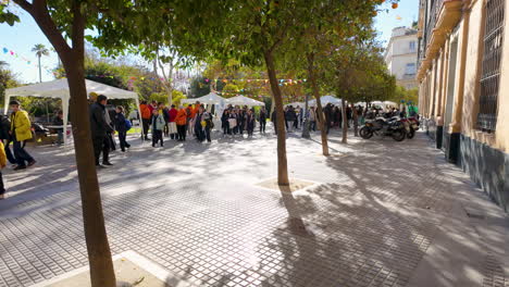 Busy-outdoor-market-under-trees-with-people-browsing-stalls-in-a-shaded-avenue