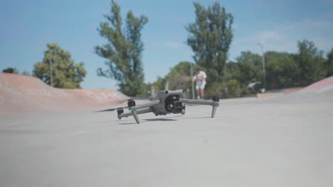 Drone-take-off-from-concrete-skatepark-ground-while-man-do-wheelie-in-background