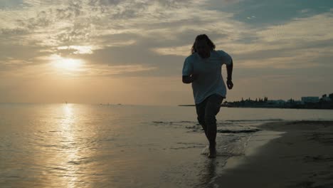mid-shot-of-young-Male-running-on-the-beach-in-the-water-at-sunrise-slow-motion